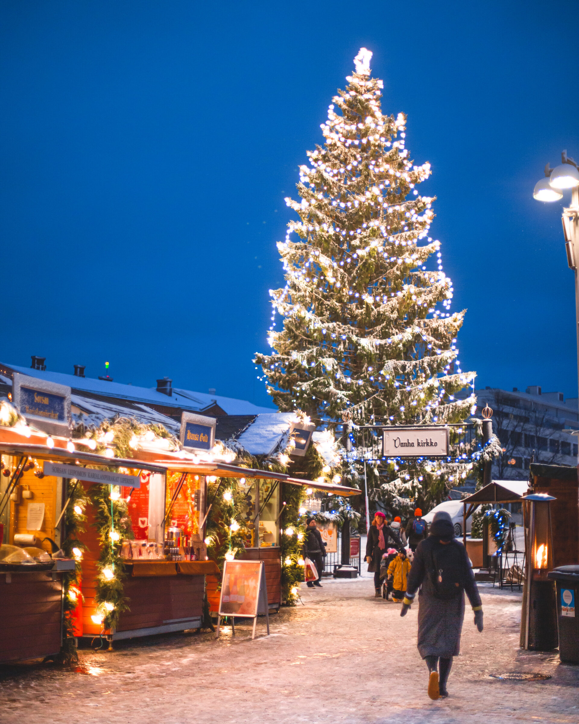 Keskustorin valaistu joulukuusi ja joulutorin punaisia myyntikojuja.